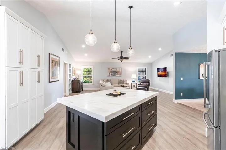 Kitchen featuring open floor plan, white cabinetry, lofted ceiling, light wood finished floors, and freestanding refrigerator