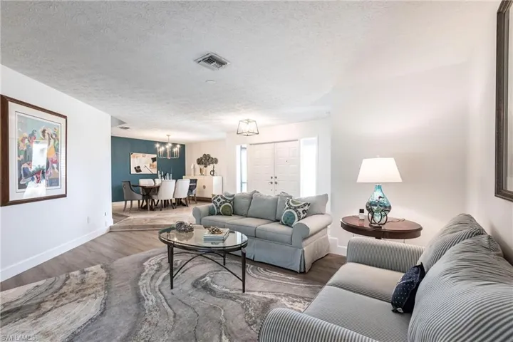 Living area featuring baseboards, a chandelier, a textured ceiling, visible vents, and wood finished floors