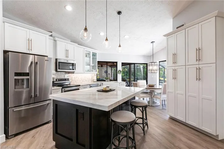 Kitchen with light wood-type flooring, stainless steel appliances, a breakfast bar, a kitchen island, and light stone counters