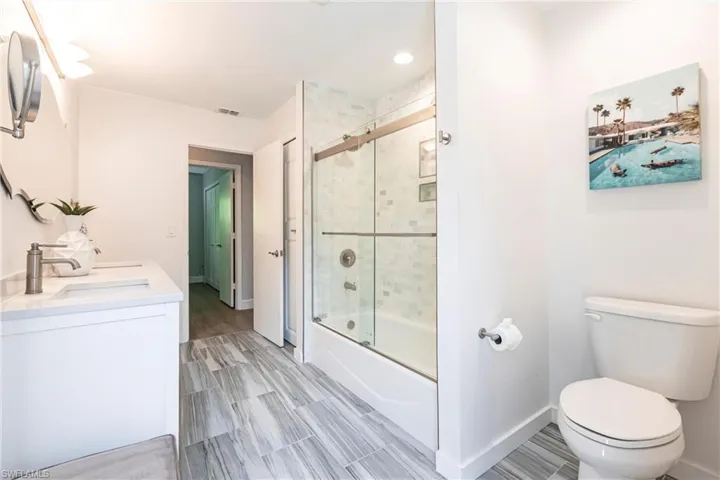 Bathroom with baseboards, double vanity, toilet, a sink, and shower / bath combination with glass door