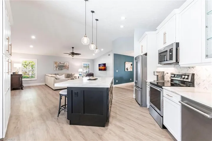 Kitchen featuring a kitchen island, open floor plan, lofted ceiling, stainless steel appliances, and white cabinets