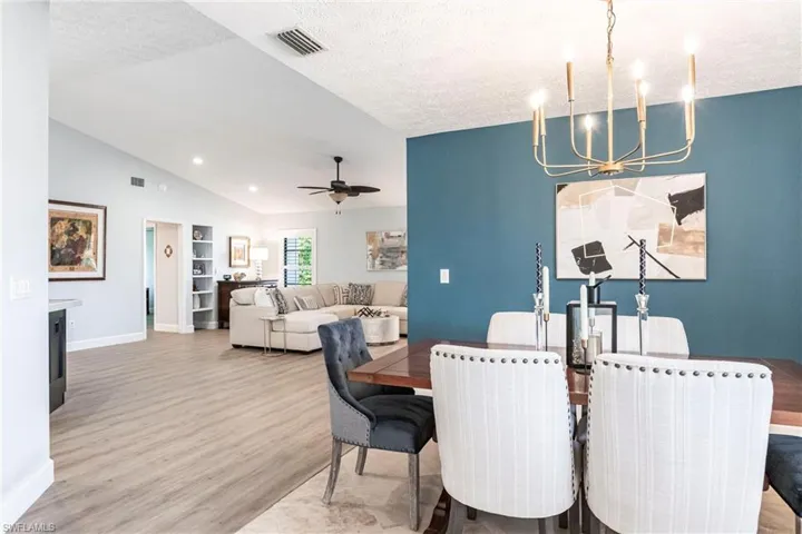 Dining space featuring lofted ceiling, ceiling fan with notable chandelier, a textured ceiling, visible vents, and wood finished floors