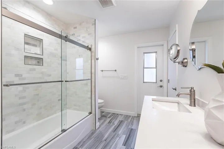 Full bath with vanity, toilet, baseboards, bath / shower combo with glass door, and visible vents