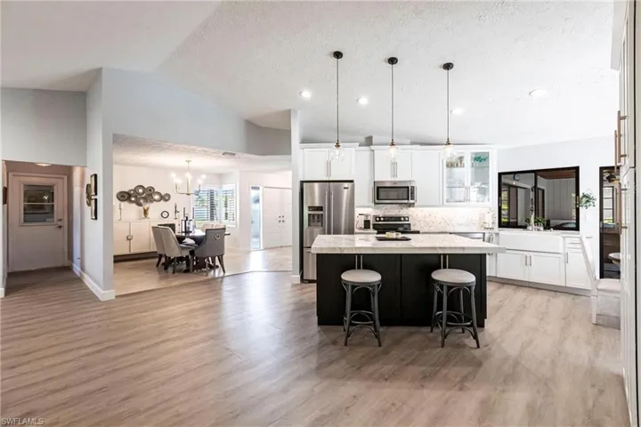 Kitchen with light wood-style flooring, stainless steel appliances, a center island, an inviting chandelier, and backsplash