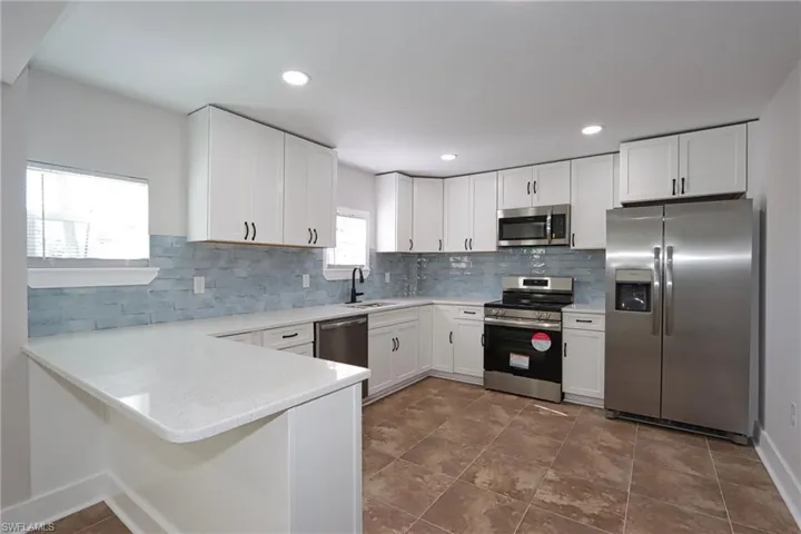 Kitchen with stainless steel appliances, a peninsula, white cabinets, light stone counters, and recessed lighting