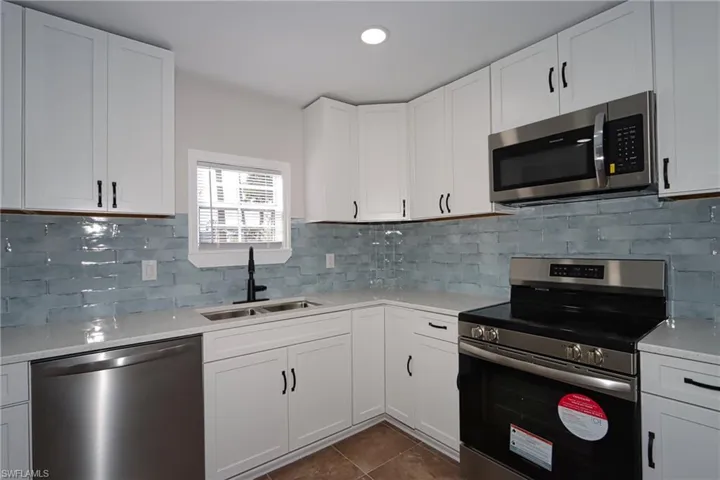 Kitchen featuring stainless steel appliances, white cabinetry, dark tile patterned flooring, backsplash, and recessed lighting