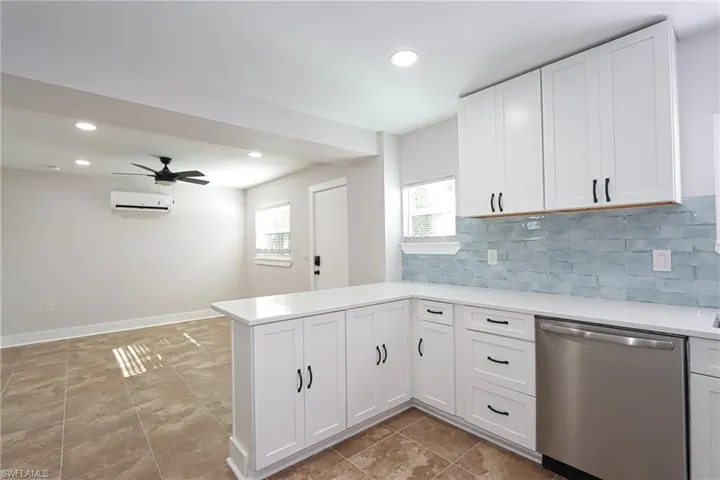 Kitchen featuring stainless steel dishwasher, a peninsula, white cabinetry, backsplash, and recessed lighting