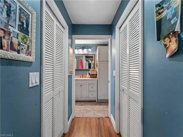 Corridor into bathroom with walk in closets with light hardwood / wood-style floors and sink