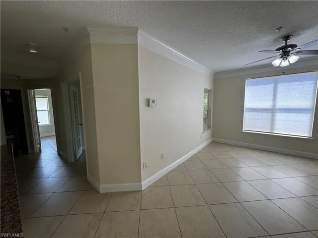Unfurnished room with ceiling fan, baseboards, a textured ceiling, light tile patterned flooring, and crown molding