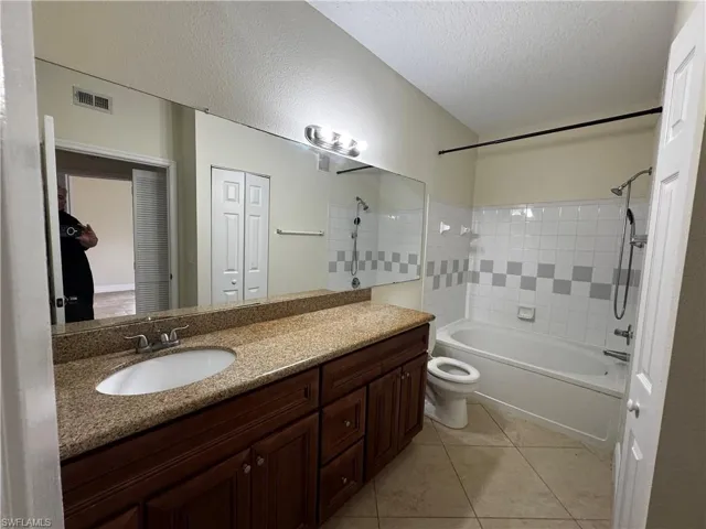 Bathroom featuring tile patterned floors, toilet, shower / bathtub combination, vanity, and a textured ceiling