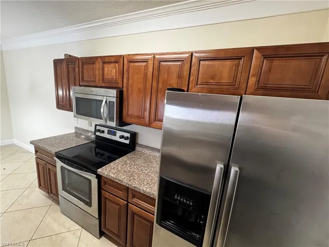 Kitchen featuring light tile patterned floors, stainless steel appliances, brown cabinetry, and crown molding