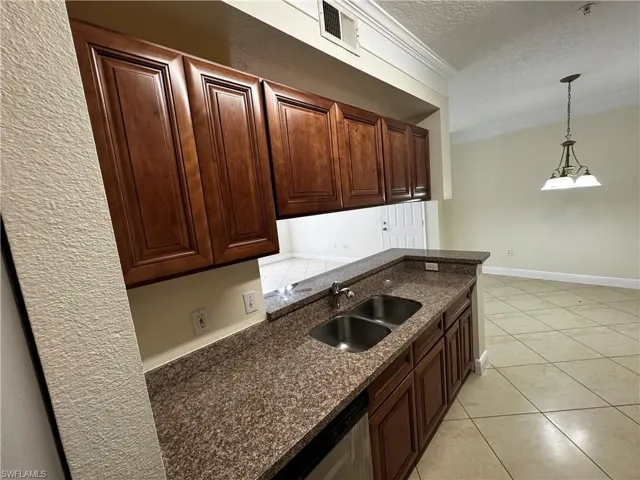 Kitchen with a textured ceiling, crown molding, a sink, visible vents, and hanging light fixtures
