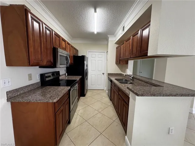 Kitchen featuring appliances with stainless steel finishes, a textured ceiling, dark countertops, and a sink