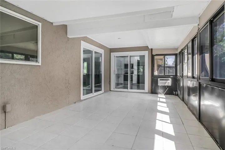 Unfurnished sunroom featuring beamed ceiling and an AC wall unit