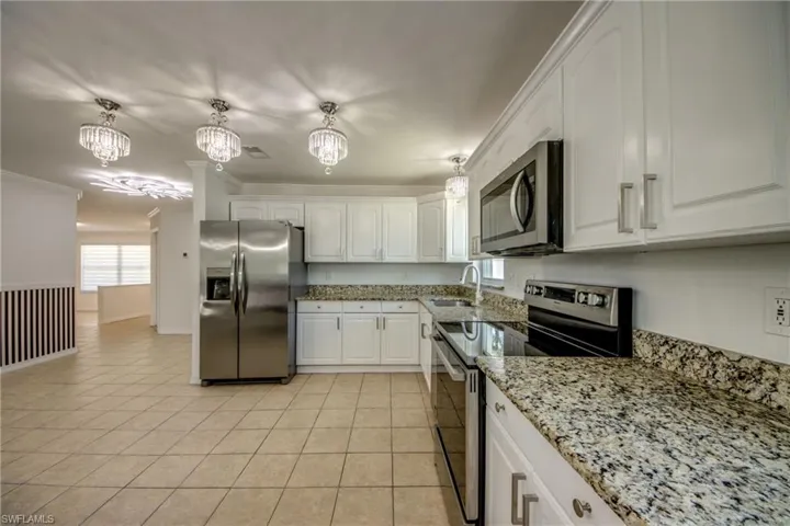 Kitchen with light stone counters, stainless steel appliances, white cabinets, hanging lights, and ornamental molding