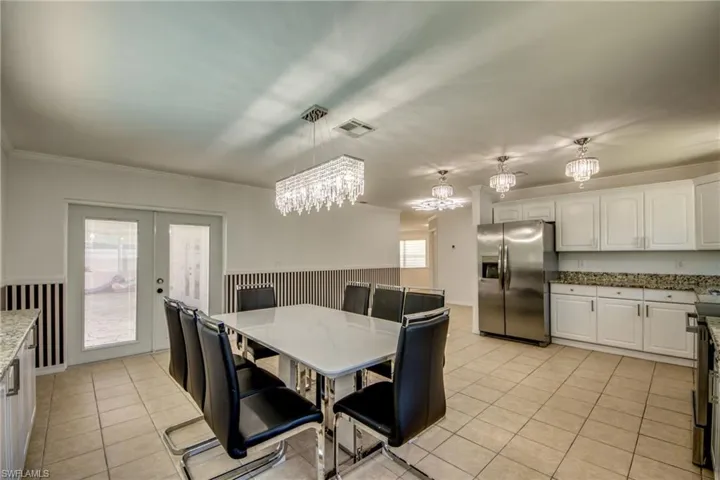 Dining room featuring french doors, a chandelier, light tile patterned flooring, ornamental molding, and a wainscoted wall