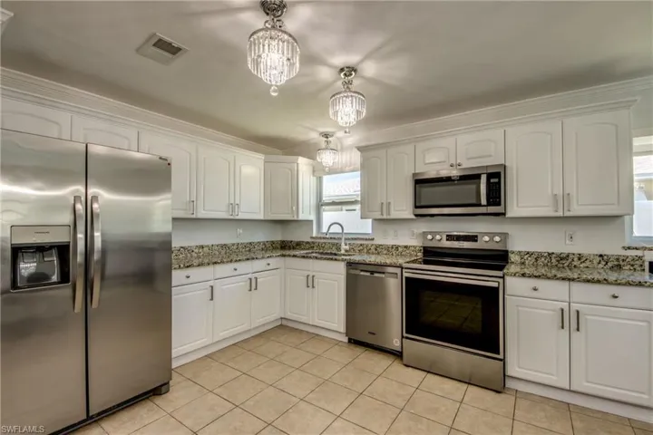 Kitchen featuring stainless steel appliances, white cabinets, suspended lighting, dark stone countertops, and ornamental molding