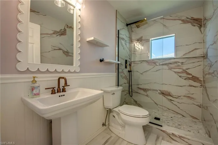 Bathroom with a marble finish shower and a wainscoted wall