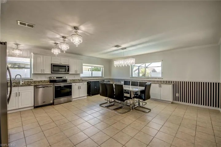 Kitchen featuring hanging lights, stainless steel appliances, white cabinets, dark stone countertops, and crown molding