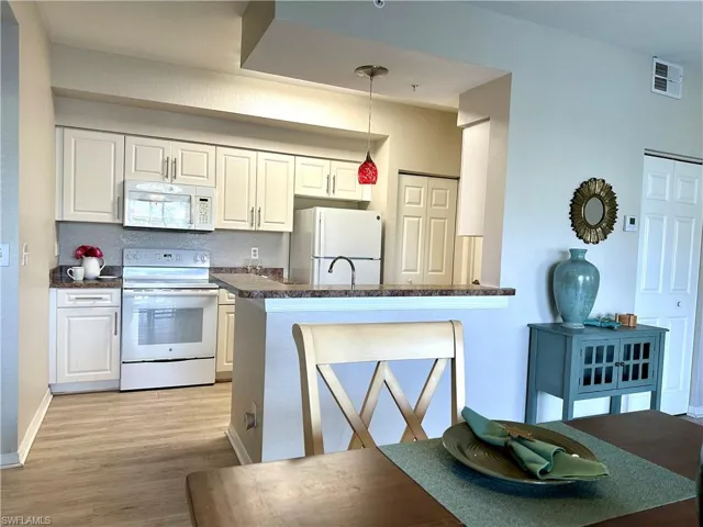 The kitchen has white cabinetry and appliances, a pantry, and a sink in the peninsula.  To the right of the pantry door is the entrance to the laundry room.
