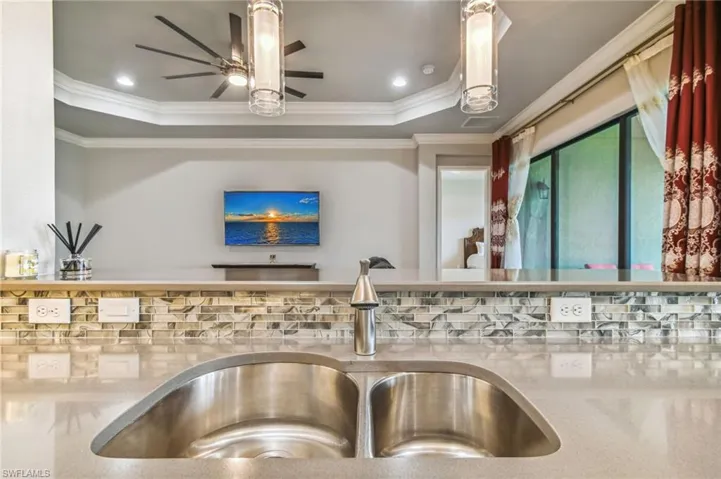 Kitchen view of light stone countertops, a raised ceiling, crown molding, a ceiling fan, and recessed lighting