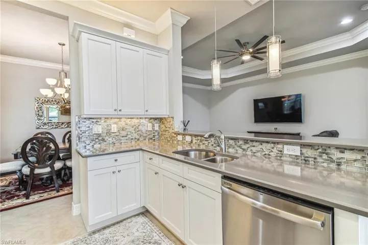 Kitchen with tasteful backsplash, ornamental molding, dishwasher, a chandelier, and white cabinets