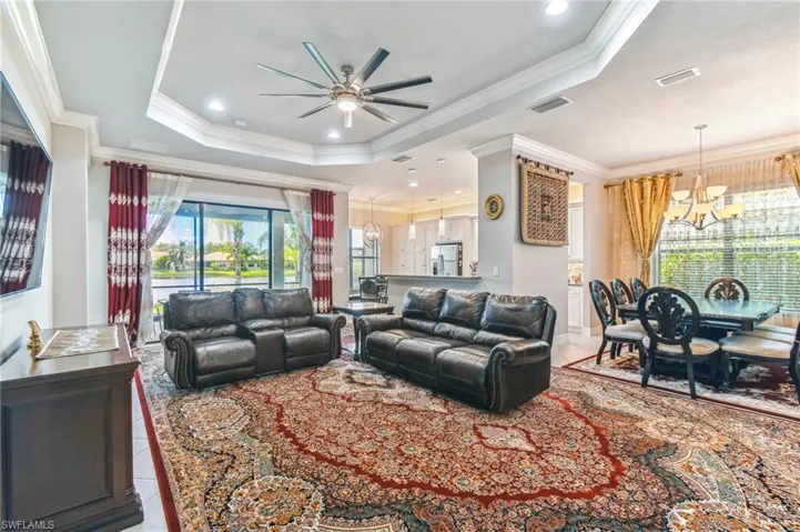 Living room with suspended lighting, light tile patterned floors, a ceiling fan, crown molding, and a raised ceiling