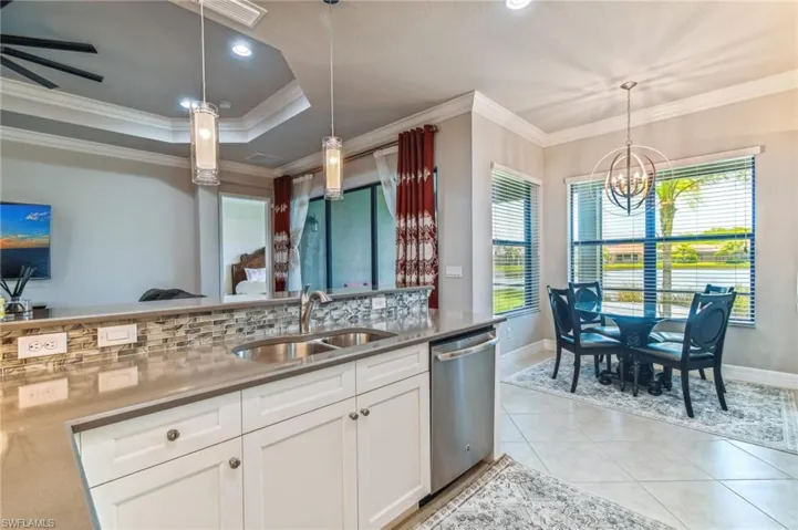Kitchen featuring ornamental molding, white cabinets, stainless steel dishwasher, light tile patterned floors, and a chandelier