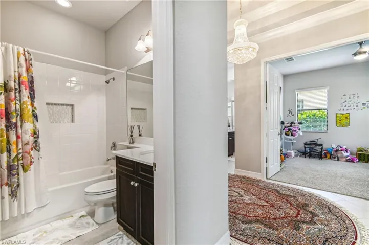 Bathroom with shower / tub combo with curtain, vanity, light tile patterned floors, and a chandelier