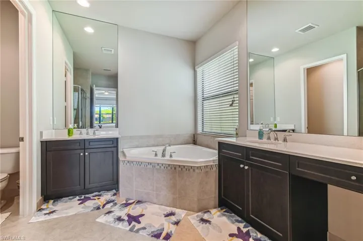 Full bathroom with two vanities, recessed lighting, a garden tub, light tile patterned floors, and a stall shower