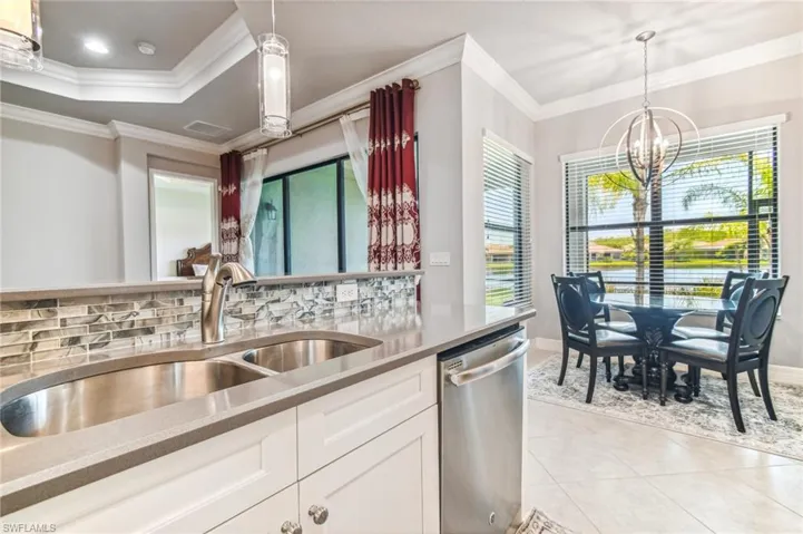 Kitchen featuring ornamental molding, dishwasher, suspended lighting, light tile patterned floors, and light stone counters