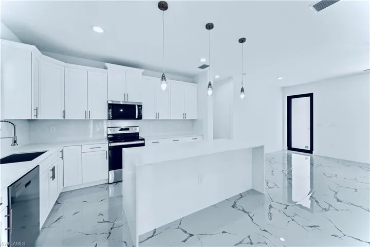 Kitchen with sink, hanging light fixtures, appliances with stainless steel finishes, a kitchen island, and white cabinets