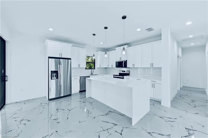 Kitchen featuring decorative light fixtures, a center island, stainless steel appliances, decorative backsplash, and white cabinets