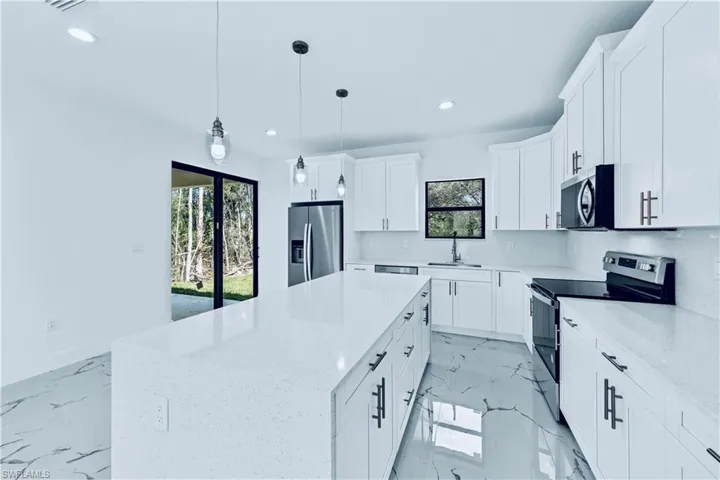 Kitchen with white cabinets, hanging light fixtures, a center island, light stone counters, and stainless steel appliances