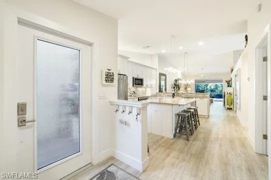 Kitchen with a kitchen island, white cabinetry, a kitchen bar, hanging light fixtures, and stainless steel appliances