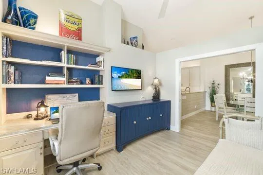 Office with lofted ceiling, an inviting chandelier, and light wood-type flooring