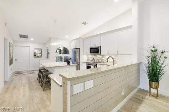 Kitchen featuring a breakfast bar area, appliances with stainless steel finishes, white cabinetry, a kitchen island, and kitchen peninsula