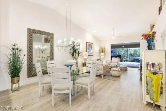 Dining room with high vaulted ceiling, ceiling fan with notable chandelier, and light hardwood / wood-style floors