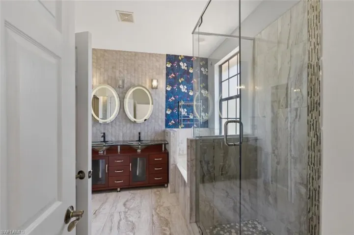 Bathroom with double vanity, a marble finish shower, a garden tub, and light marble finish flooring
