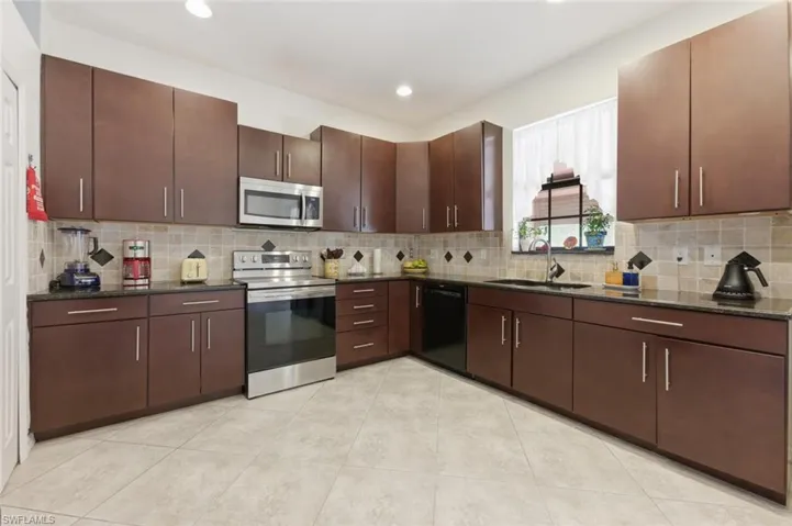 Kitchen with stainless steel appliances, dark stone countertops, dark wood finish cabinets, light tile patterned floors, and backsplash