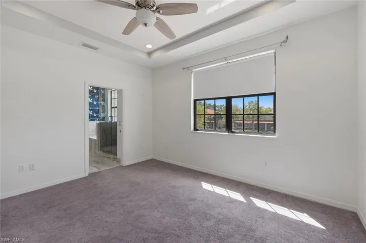 Carpeted empty room featuring a ceiling fan and a raised ceiling