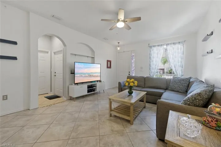 Living area with ceiling fan, arched walkways, and light tile patterned floors