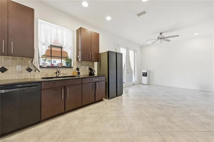 Kitchen featuring dark wood finish cabinetry, black appliances, dark stone counters, plenty of natural light, and recessed lighting