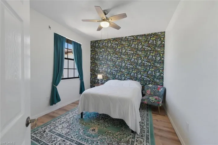 Bedroom with an accent wall, wallpapered walls, light wood-style flooring, and a ceiling fan