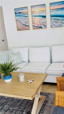 Bright living area featuring a light-toned wood-finish coffee table, white sofa with light blue piping, and a dark patterned area rug