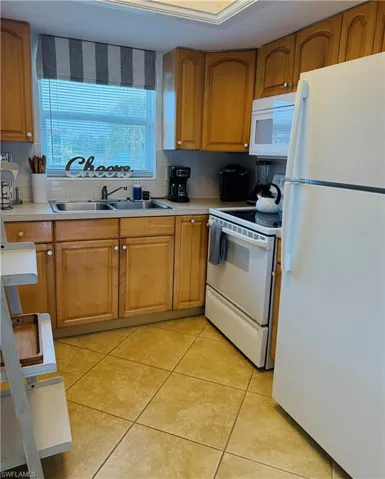 Kitchen featuring wood cabinetry, a double basin stainless steel sink, tile flooring, and white appliances including a refrigerator, range, and microwave