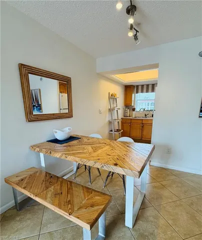 Dining area featuring tile flooring, a track lighting fixture, and a pass-through opening to the kitchen with wood cabinetry