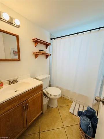 Bathroom featuring a wood-finish vanity with a built-in sink, a white shower curtain, and contrasting wall shelving