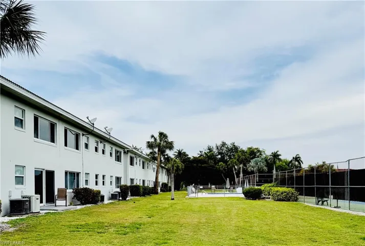Expansive lawn area featuring a tennis court with chain-link fencing, a swimming pool with surrounding deck, and multiple palm trees