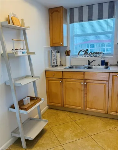 Kitchen area featuring a double basin stainless steel sink, light wood-finish cabinetry, a ceramic tile backsplash, and tile flooring